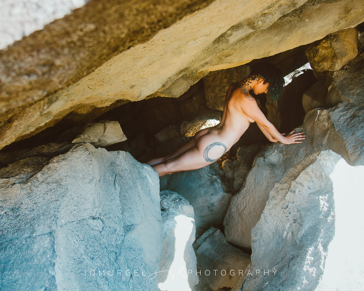 nude woman curled up on rocks